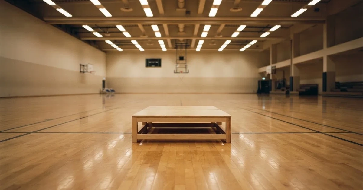 Ein Podium aus hellem Holz steht in einer leeren Sporthalle unter Hallenlicht, ohne Beschriftung oder Zahlen, niemand ist zu sehen.